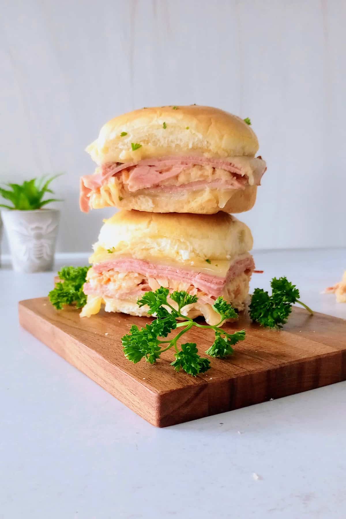 Baked Reuben sliders fresh out of the oven. Stacked on top of each other on a dark brown cutting board next to fresh parsley.