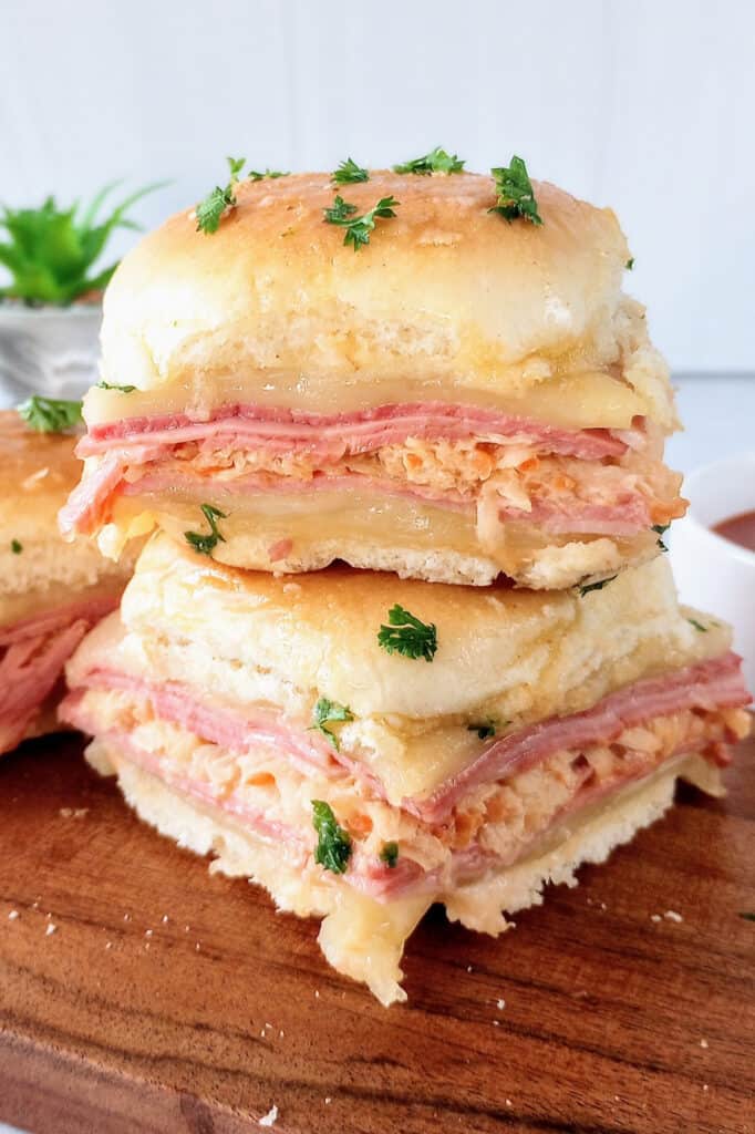 Reuben sliders on a dark brown cutting board next to fresh parsley. 