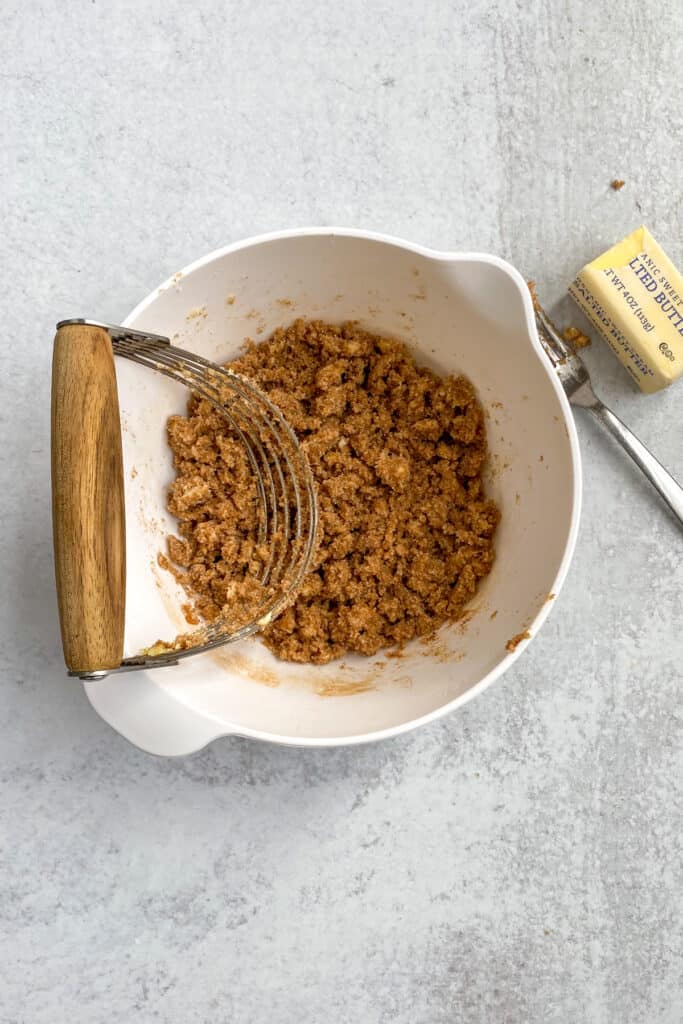 Crumbled brown sugar cinnamon crescent roll filling in a bowl with a pastry cutter sitting in bowl.