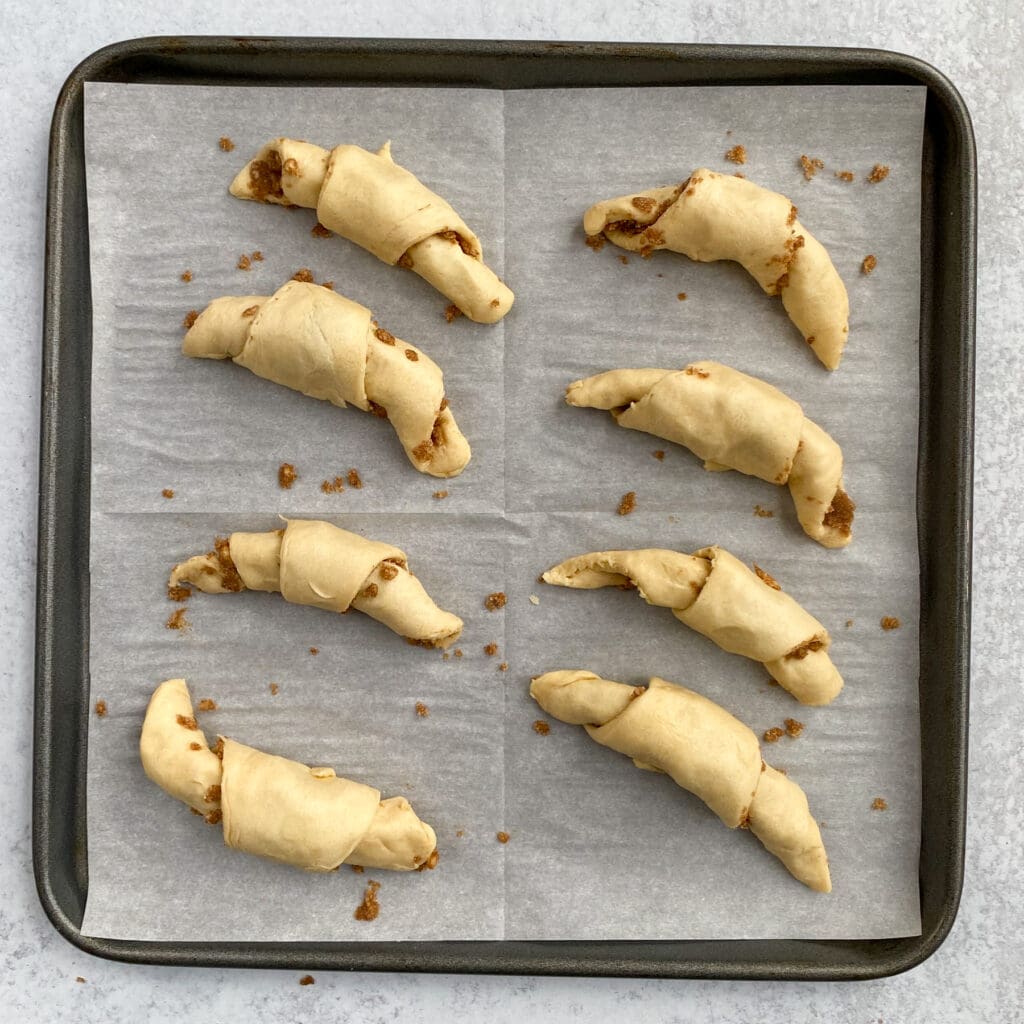 Eight cinnamon sugar crescent rolls all rolled up and ready to put in oven.