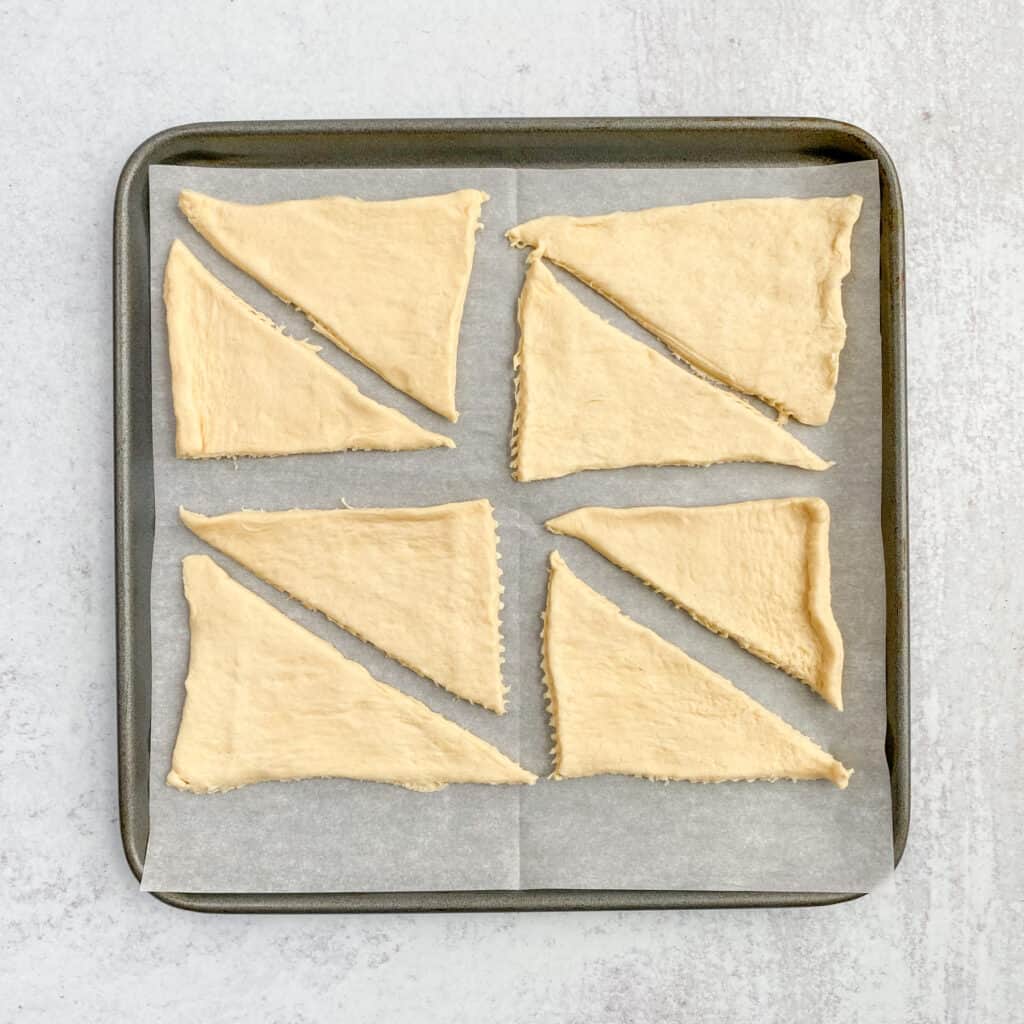 Crescent roll dough separated into eight crescents on a parchment paper lined baking sheet.