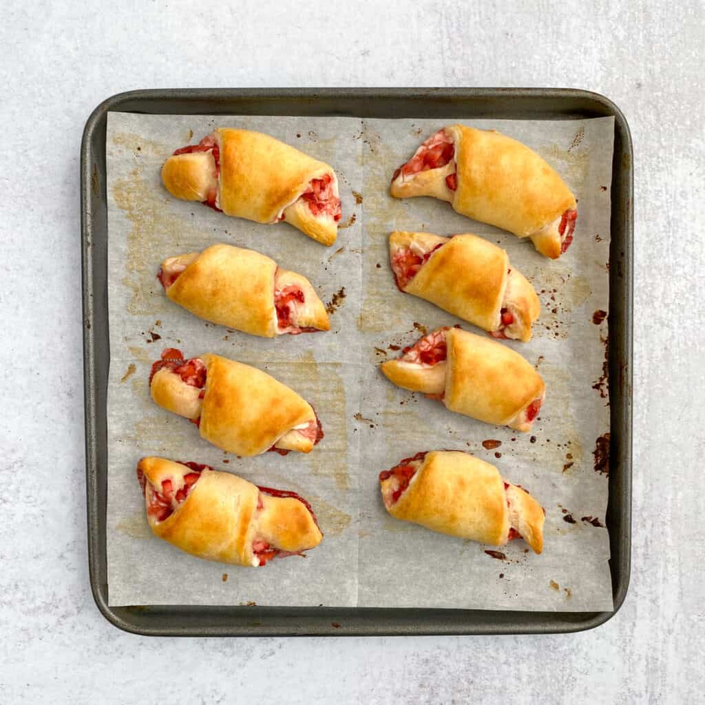 Light golden brown strawberry cream cheese crescent rolls on baking sheet just out of oven.