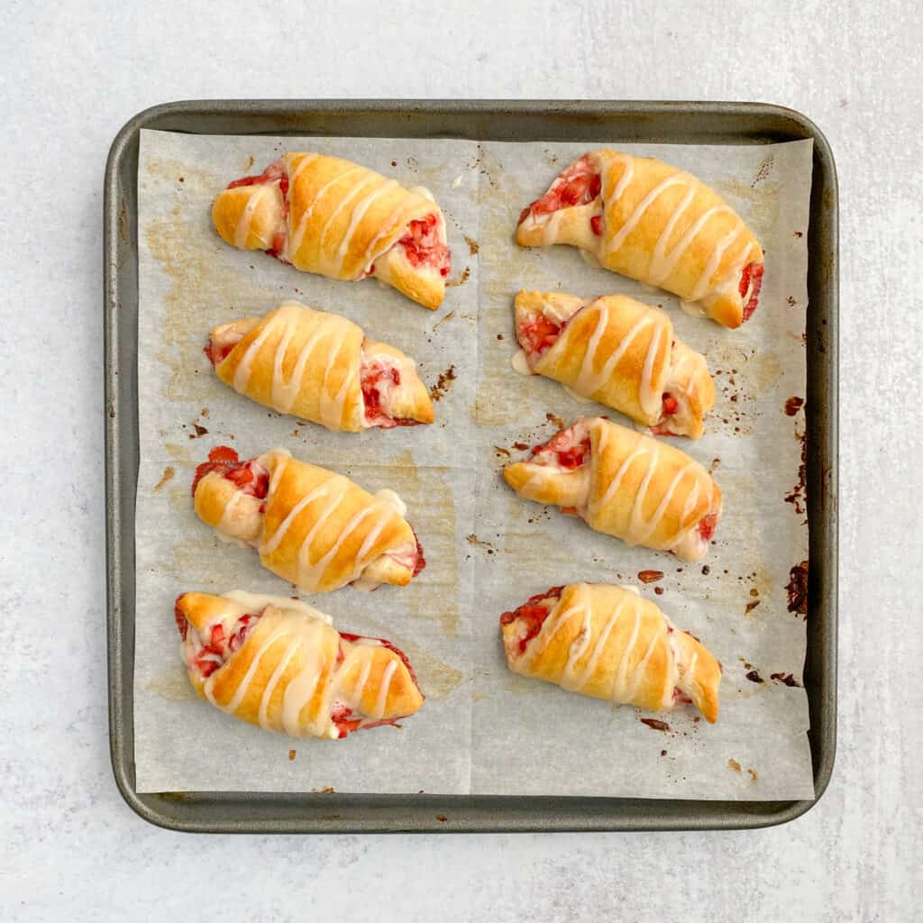 Strawberry Cream Cheese Crescent Rolls on baking sheet, with glaze drizzled on top.