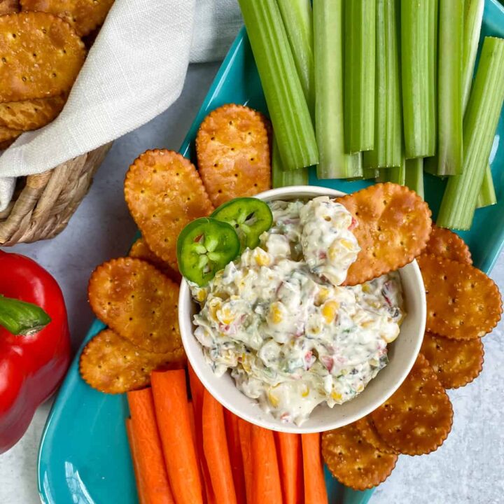 Bowl of skinny poolside dip with chip in it, on a platter of carrot and celery sticks, and pretzel chips.