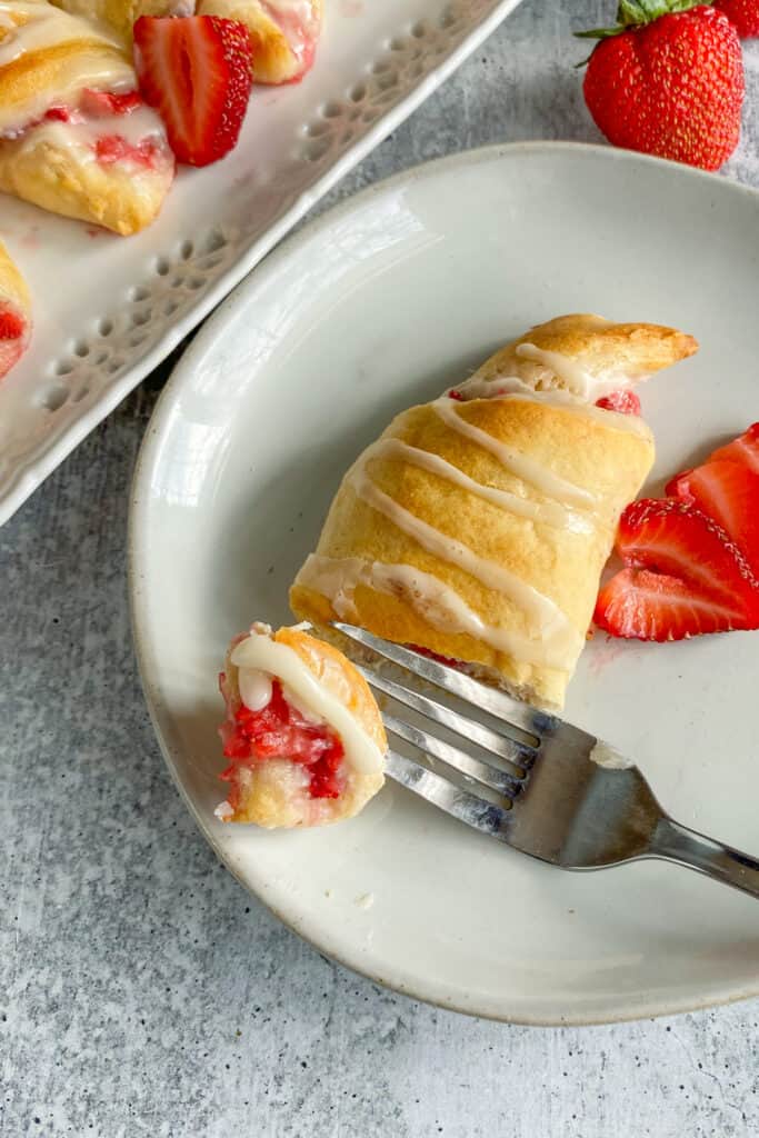 A piece of strawberry cream cheese crescent on a fork with the warm glaze dripping on it.