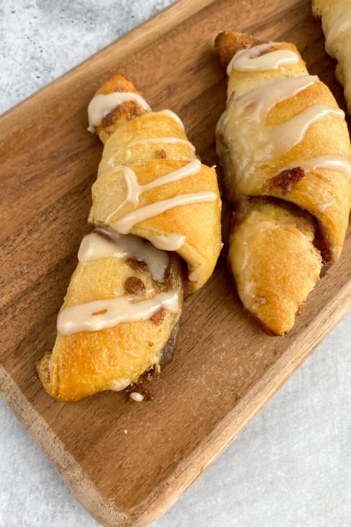 A cinnamon sugar crescent roll hot out of the oven with glaze dripping on top and the cinnamon filling dripping out.