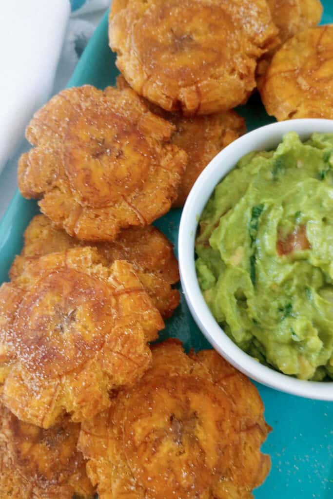 Homemade tostones on a platter with a bowl of guacamole for dipping them into.