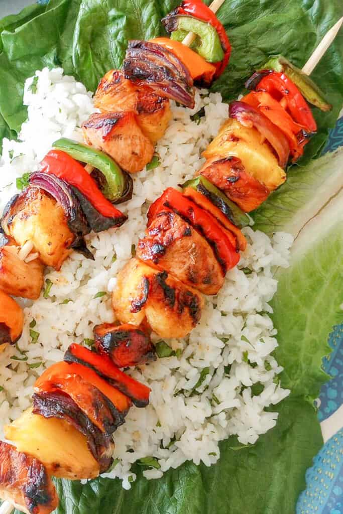 Easy Pineapple chicken kebabs on top of jasmine rice laid on top of romaine lettuce. 