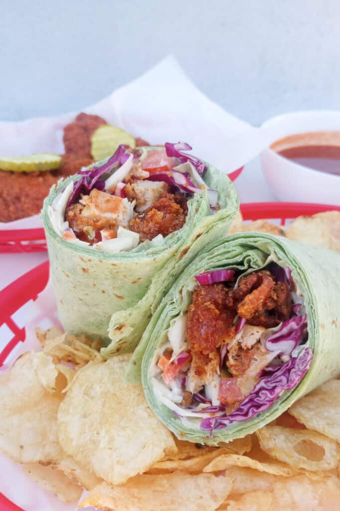 Nashville hot chicken wrap Po-boy style wrapped in a large spinach wrap filled with creamy Cole slaw, tomatoes, dill pickles, and a creamy Cajun remoulade sauce.