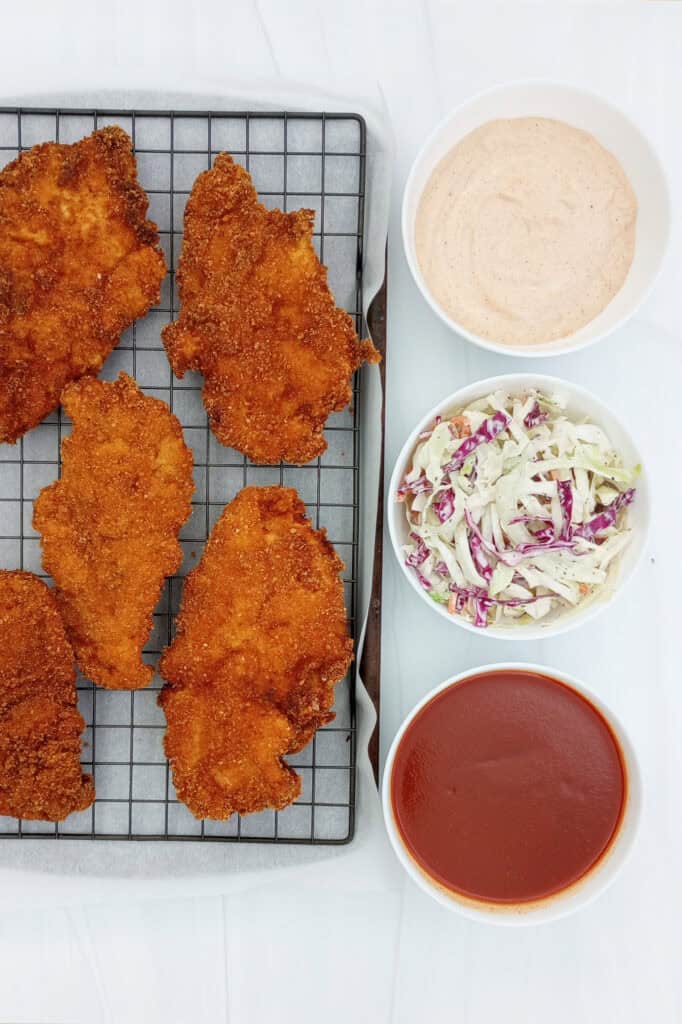 Double breaded fried chicken next to creamy Cajun sauce, Nashville hot sauce, and Cole slaw. 