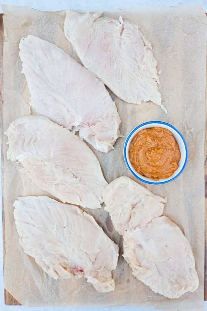 Chicken breasts flattened out next to red pesto sauce. 