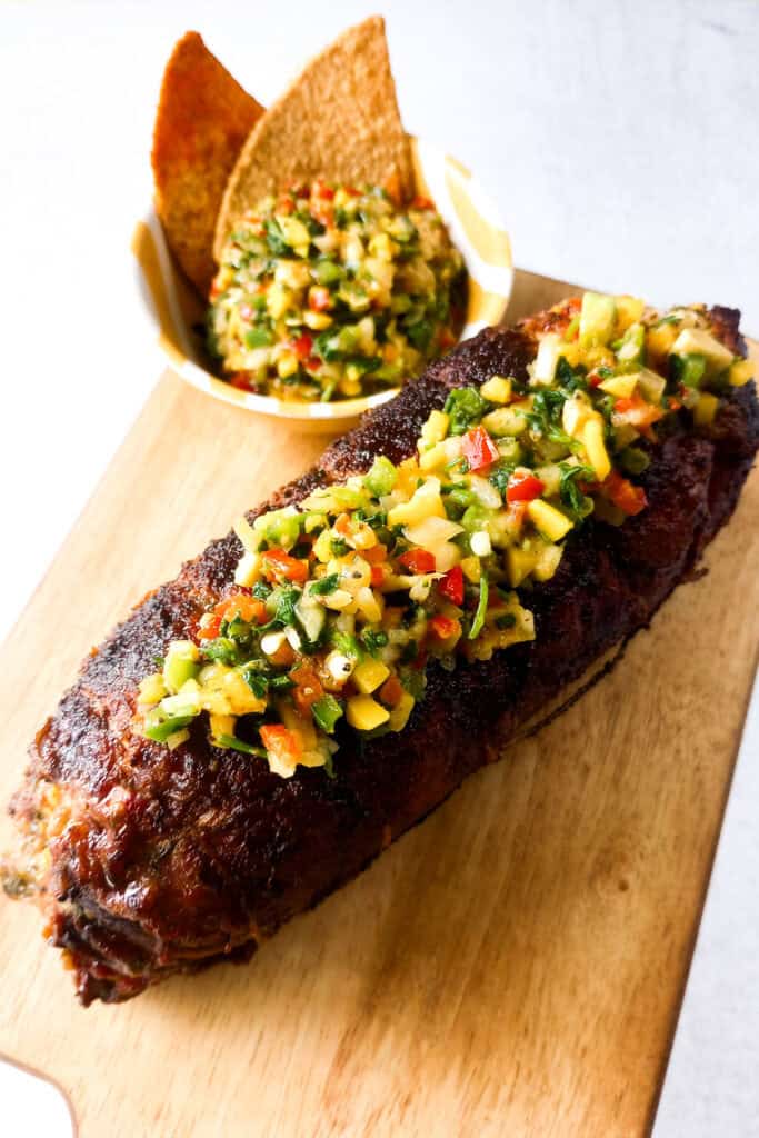 Steak roll fresh off the grill topped with mango avocado salsa next to a bowl with salsa and chips. 