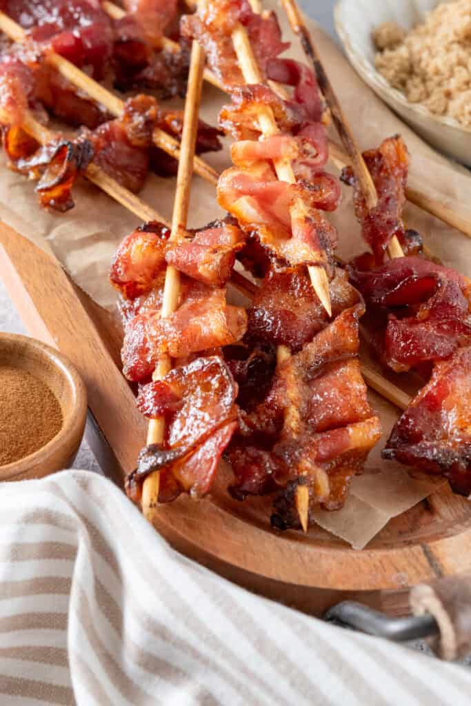 Brown sugar candied bacon on skewers on a wood serving board.