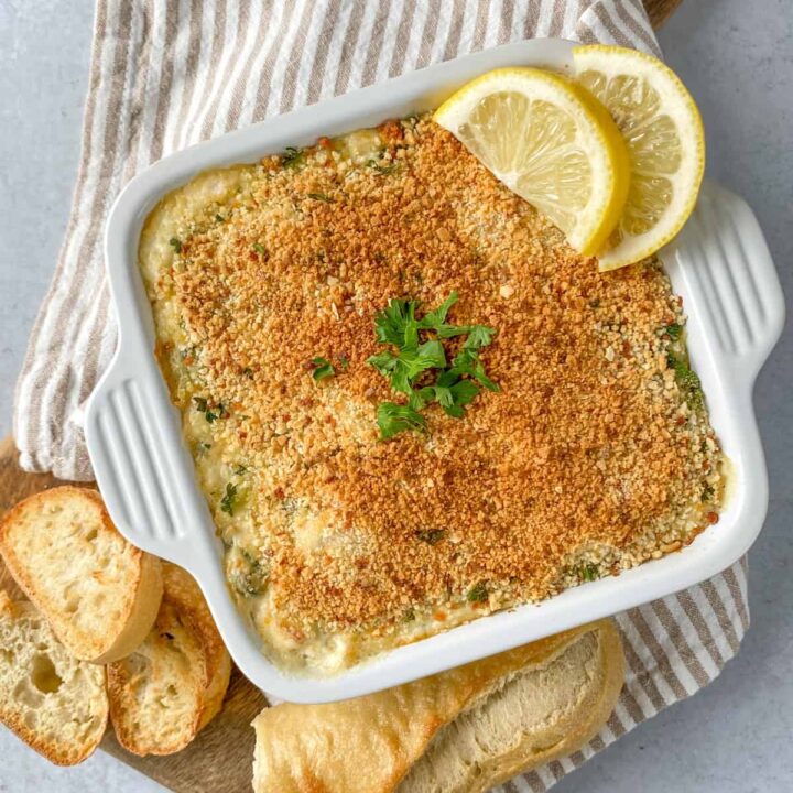 Crab and spinach dip in a square baking pan, topped with bread crumbs and garnished with lemon wedges and parsley.