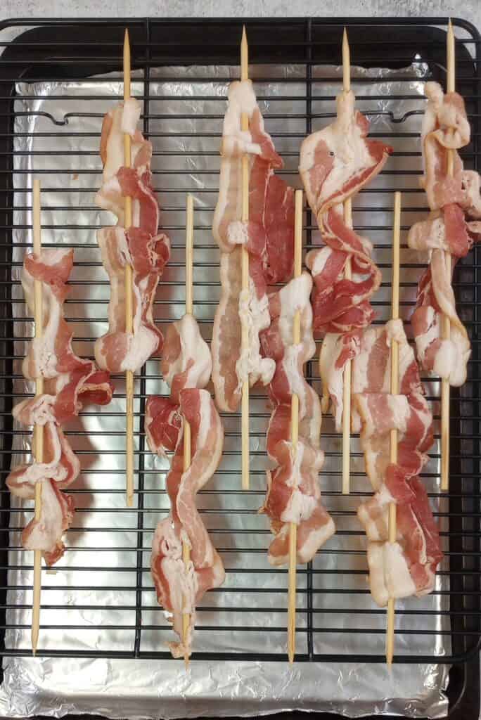 Bacon spread out evenly onto 12 inch bamboo skewers ready to be glazed with brown sugar sauce and baked.