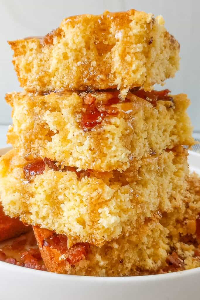 Three square pieces of bacon cornbread stacked on top of each other with maple syrup dripping down the side.