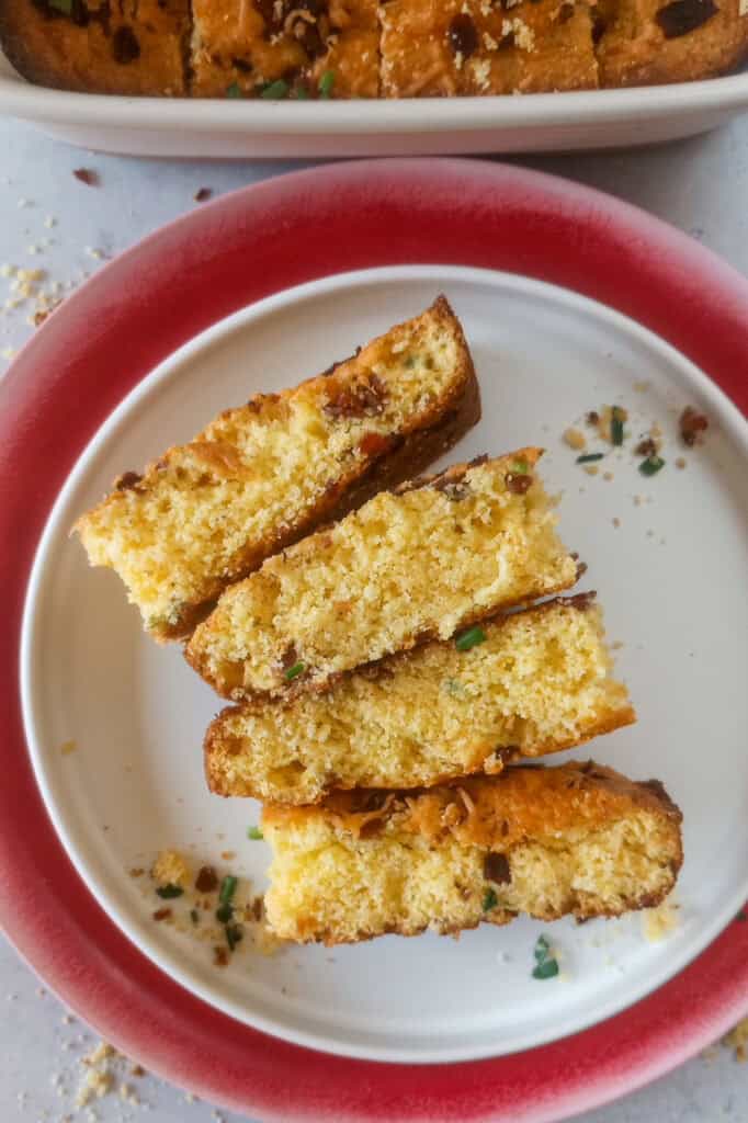 Cornbread arranged on a red plate flipped and angled with a white baking dish in the background. 