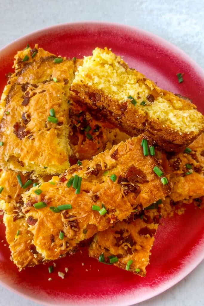 Cheddar bacon scallion cornbread on a red plate stacked overlapping. One piece of cornbread is laying on the side.