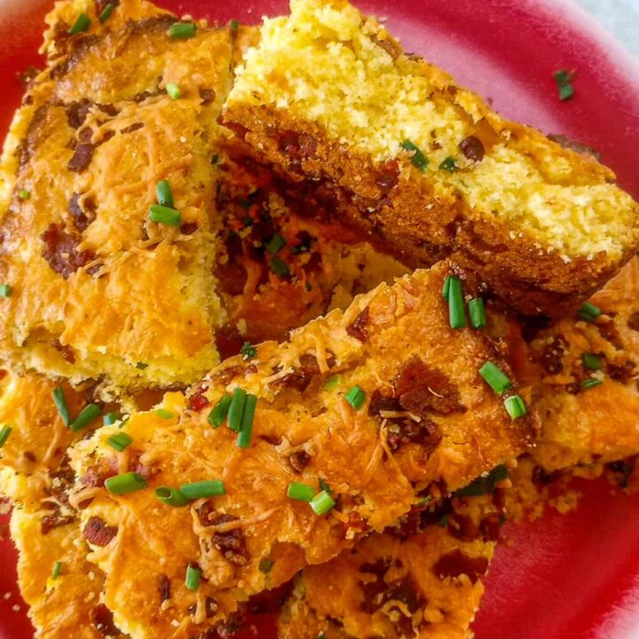 Cheddar bacon scallion cornbread on a red plate stacked overlapping. One piece of cornbread is laying on the side.