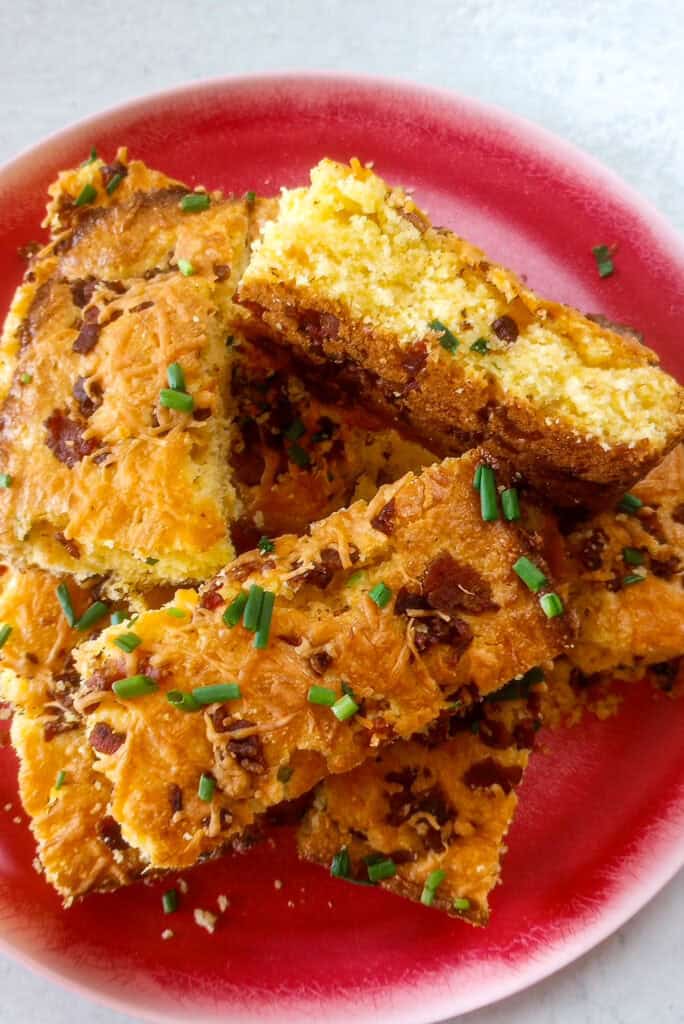 Cheddar bacon scallion cornbread on a red plate stacked overlapping. One piece of cornbread is laying on the side.