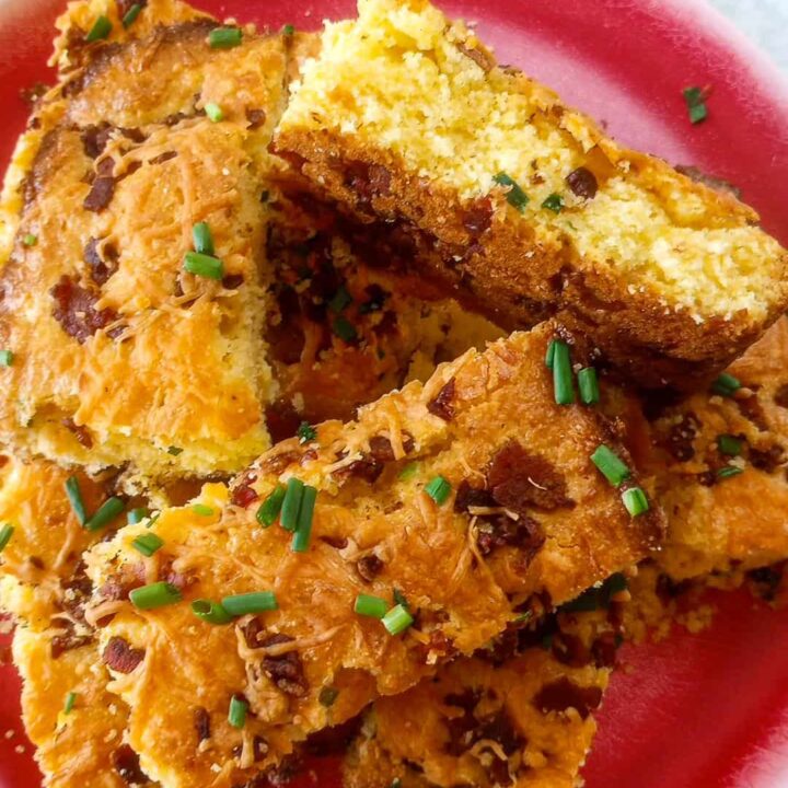 Cheddar bacon scallion cornbread on a red plate stacked overlapping. One piece of cornbread is laying on the side.