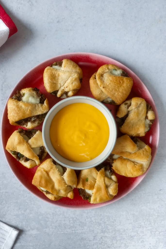 Philly cups are arranged on a red plate in a circle. Inside the circle is a bowl of cheese wiz, which is perfect for dipping!