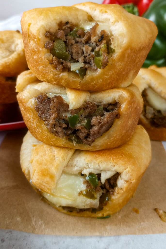 Philly cheese steak cups stacked on top of each other arranged next to a red plate.