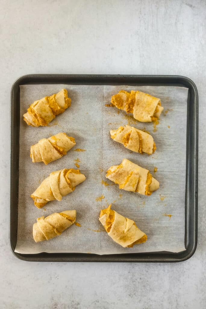 Rolled up crescent rolls sprinkled with a cinnamon sugar mixture ready to be baked in the oven. 