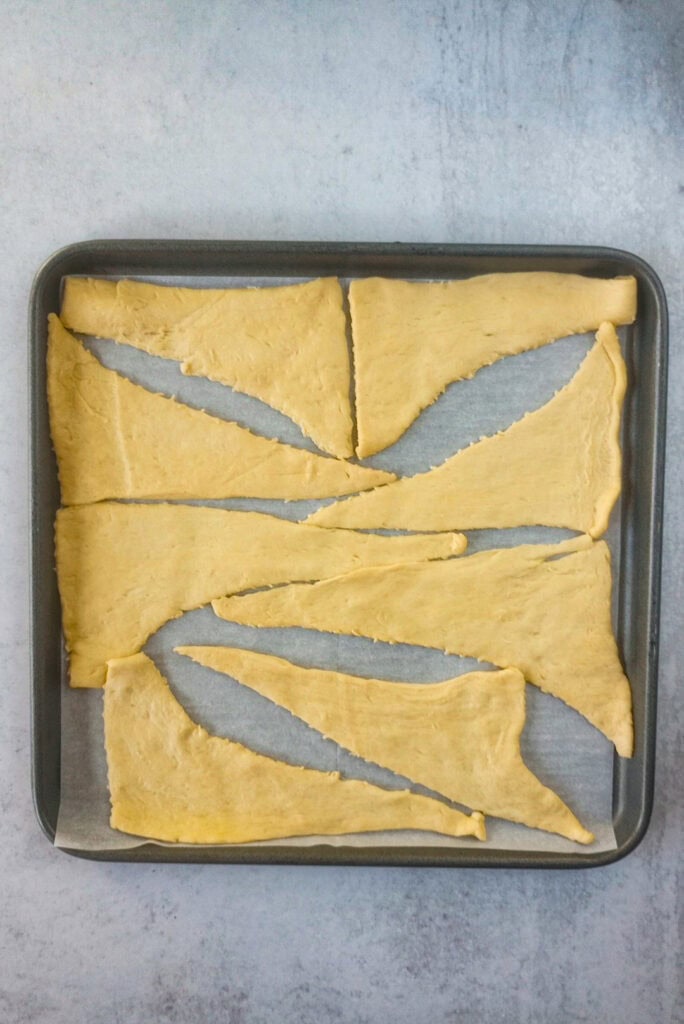 Separated Crescent rolls triangles on a baking sheet lined with parchment paper. 