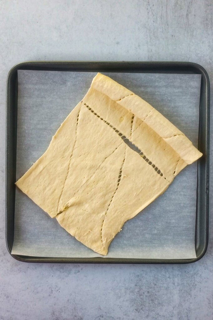 Unrolled tubed crescent roll dough on a baking sheet lined with parchment paper. 