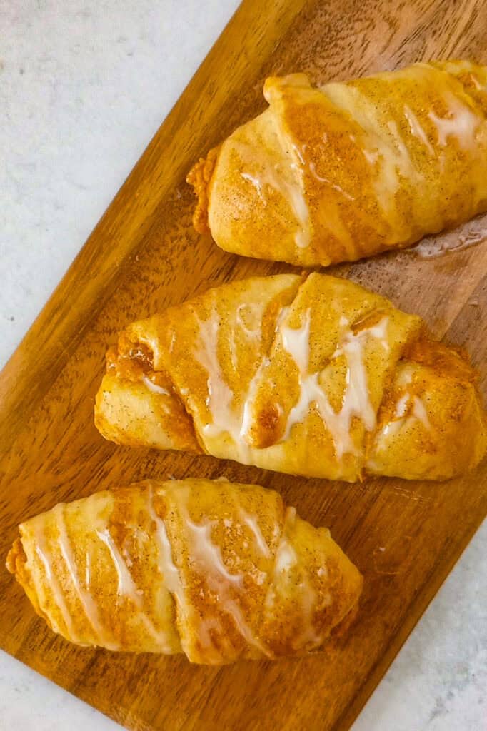 Hot pumpkin rolls fresh out of the oven on a brown chopping board drizzled with a sweet vanilla glaze. 