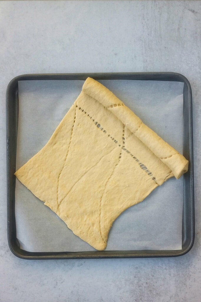 Overhead picture of crescent roll dough un-rolled on a parchment paper lined baking sheet. 