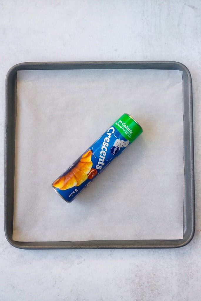 Overhead picture of Pillsbury reduced fat crescent rolls tube on a baking sheet lined with white parchment paper. 