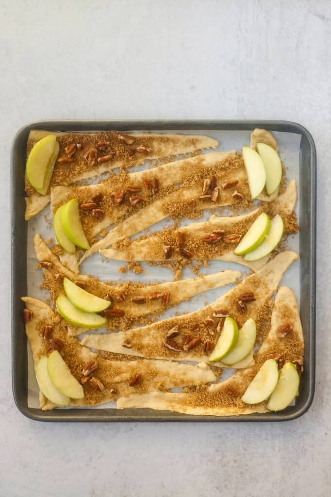 Overhead picture of cinnamon sugar rolls and green apples on the wide side ready to be rolled up. 