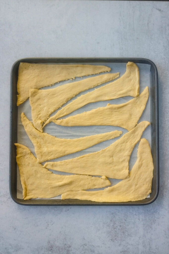 Overhead picture of crescent triangles separated on a parchment paper lined baking sheet. 