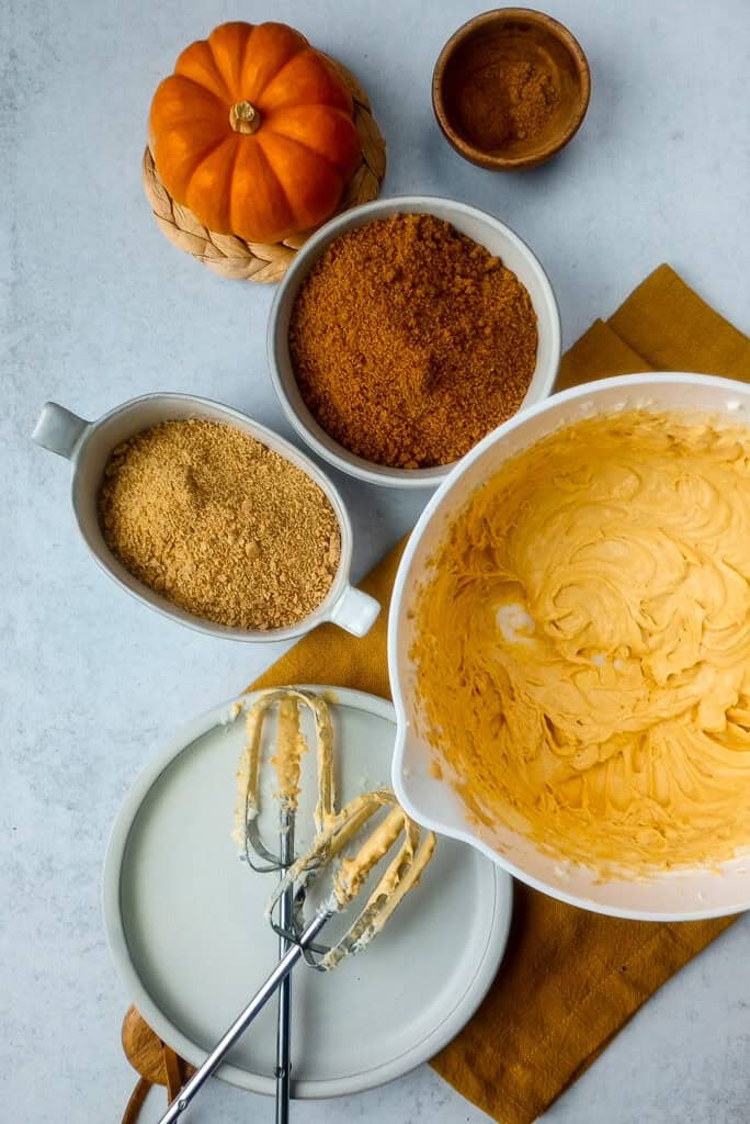 Whipped pumpkin cream cheese filling in a white bowl. Now add crumbled graham crackers and ginger snap cookies. 