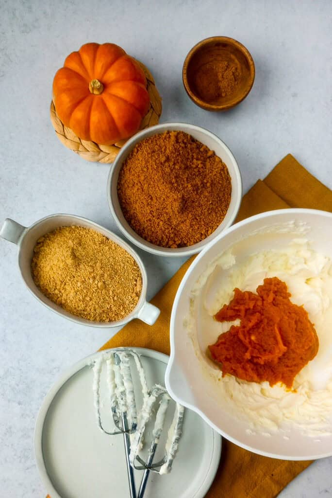 Whipped cream cheese and powdered sugar in a white mixing bowl with added pumpkin puree and spices, ready to be blended. 