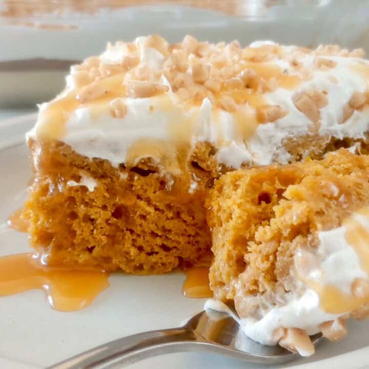 A slice of pumpkin poke cake with whipped cream, caramel and toffee topping on a plate with a fork.