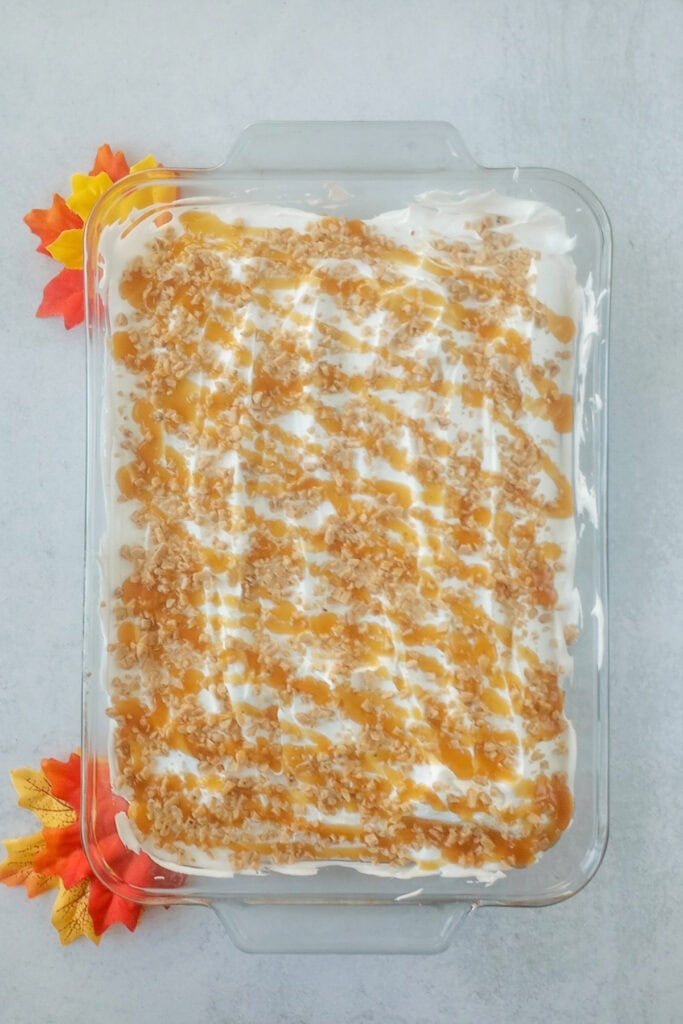 Overhead picture of a 9x13 pumpkin poke cake in baking pan, covered with Cool Whip, Heath toffee bits and caramel sauce.