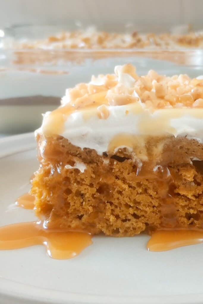 Up close picture of pumpkin poke cake topped with cool whip, toffee bits and drizzled with caramel syrup. 