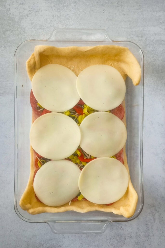 Overhead picture of cheese, meat, pesto sauce and seasonings, topped with provolone cheese. 