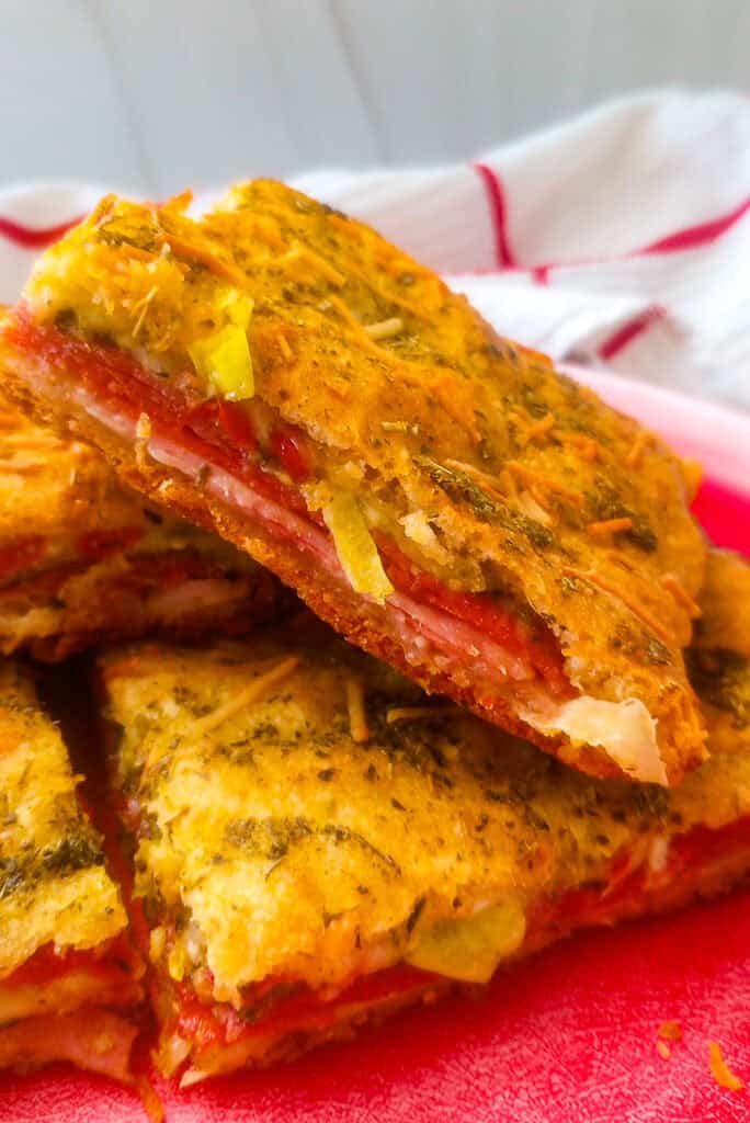 Picture of antipasto squares stacked on a red plate with a red and white checkered towel in the background. 