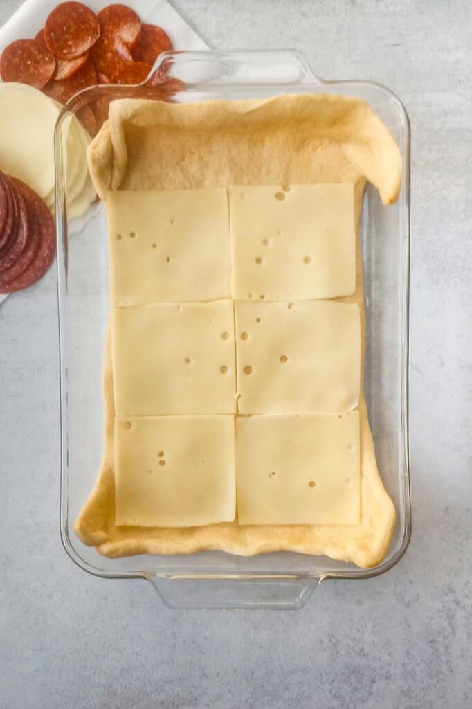 Overhead picture of crescent roll dough layered with sliced Swiss cheese. 