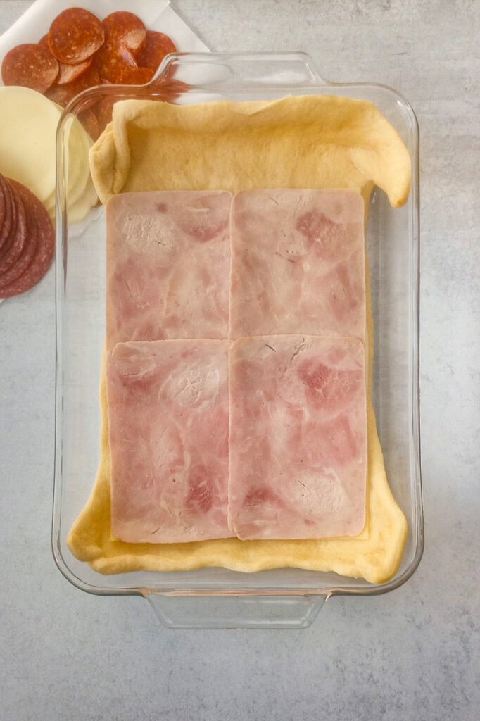 Overhead picture of crescent roll dough topped with sliced deli ham.