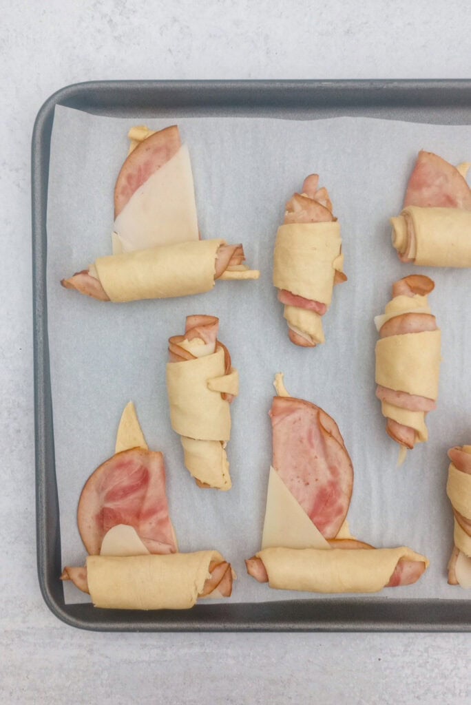 Overhead picture of ham and cheese crescent rolls showing how to roll ham and cheese sticks. You start at the wide end, tuck in the bottom and roll upward towards the triangular end. 