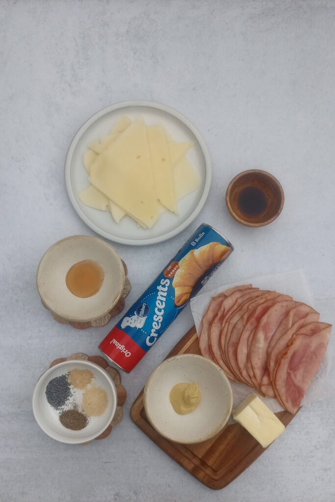 Overhead picture of Pillsbury Canned crescent rolls, sliced ham, Swiss cheese, Dijon mustard, honey, poppy seeds, garlic powder, onion powder, black pepper and Worcestershire sauce. 