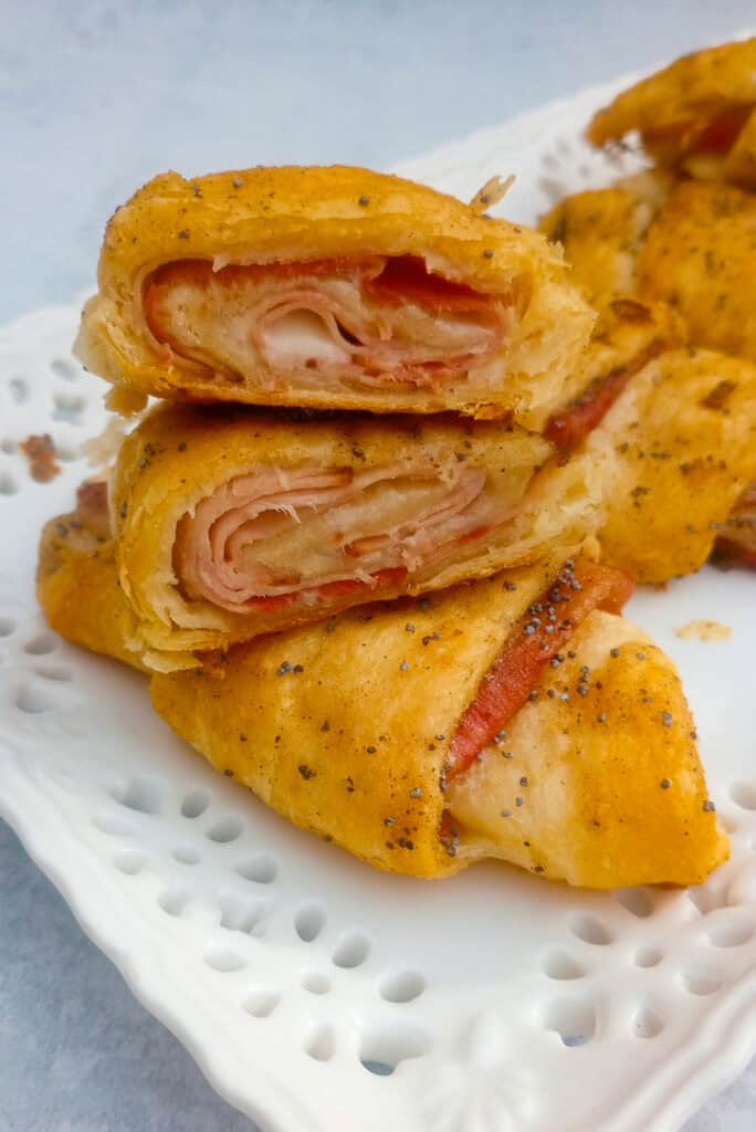 Up close picture of ham and cheese crescent rolls. One roll is sliced in half and stacked on a whole crescent roll to show the inside of bubbly, gooey, Swiss cheese and ham.