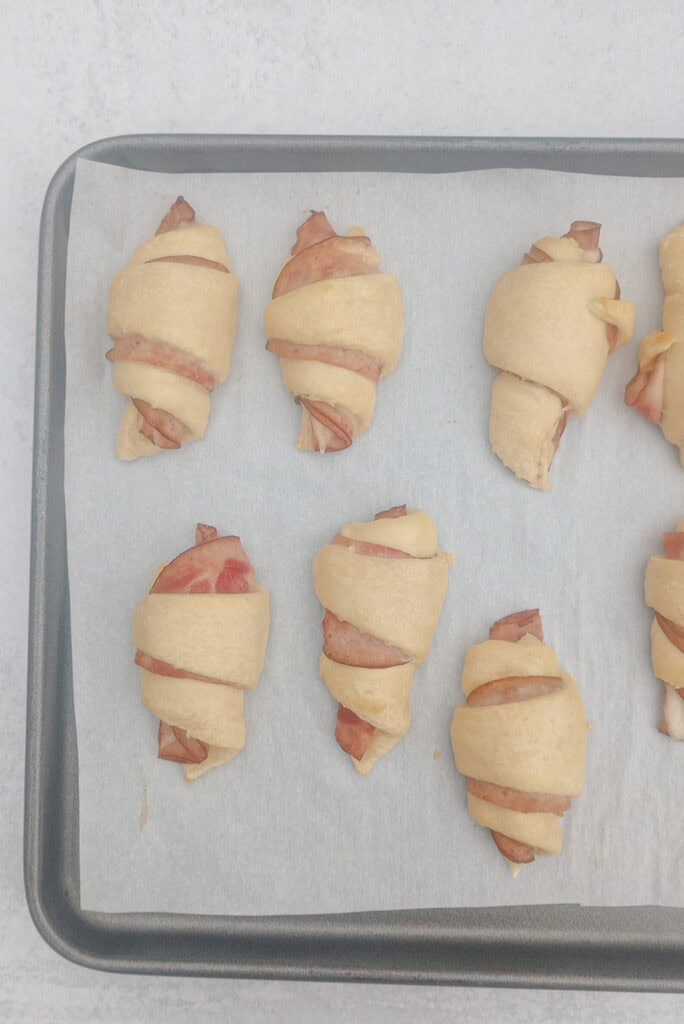 Overhead picture of ham and cheese roll-ups on a baking sheet ready to be baked for 7 minutes before brushing with honey Dijon glaze sauce. 