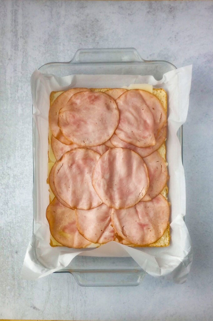 Overhead picture of Hawaiian rolls layered with Swiss cheese and sliced ham. 