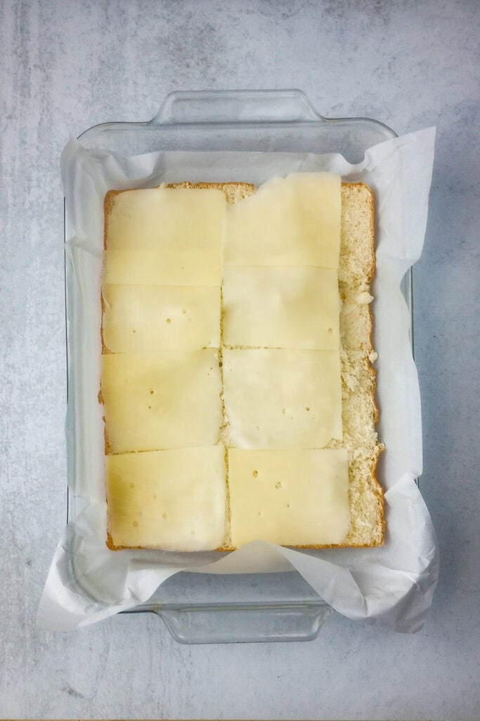 Overhead picture of Hawaiian rolls layered with the first layer of Swiss cheese. 